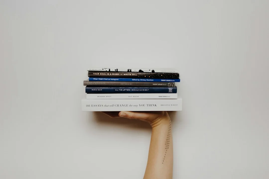 A hand holding a small stack of books against a pale wall